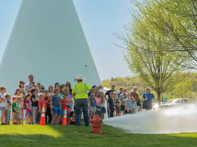 RPU staff demonstrates a fire hydrant to a group of community members near a water tower during a public event.